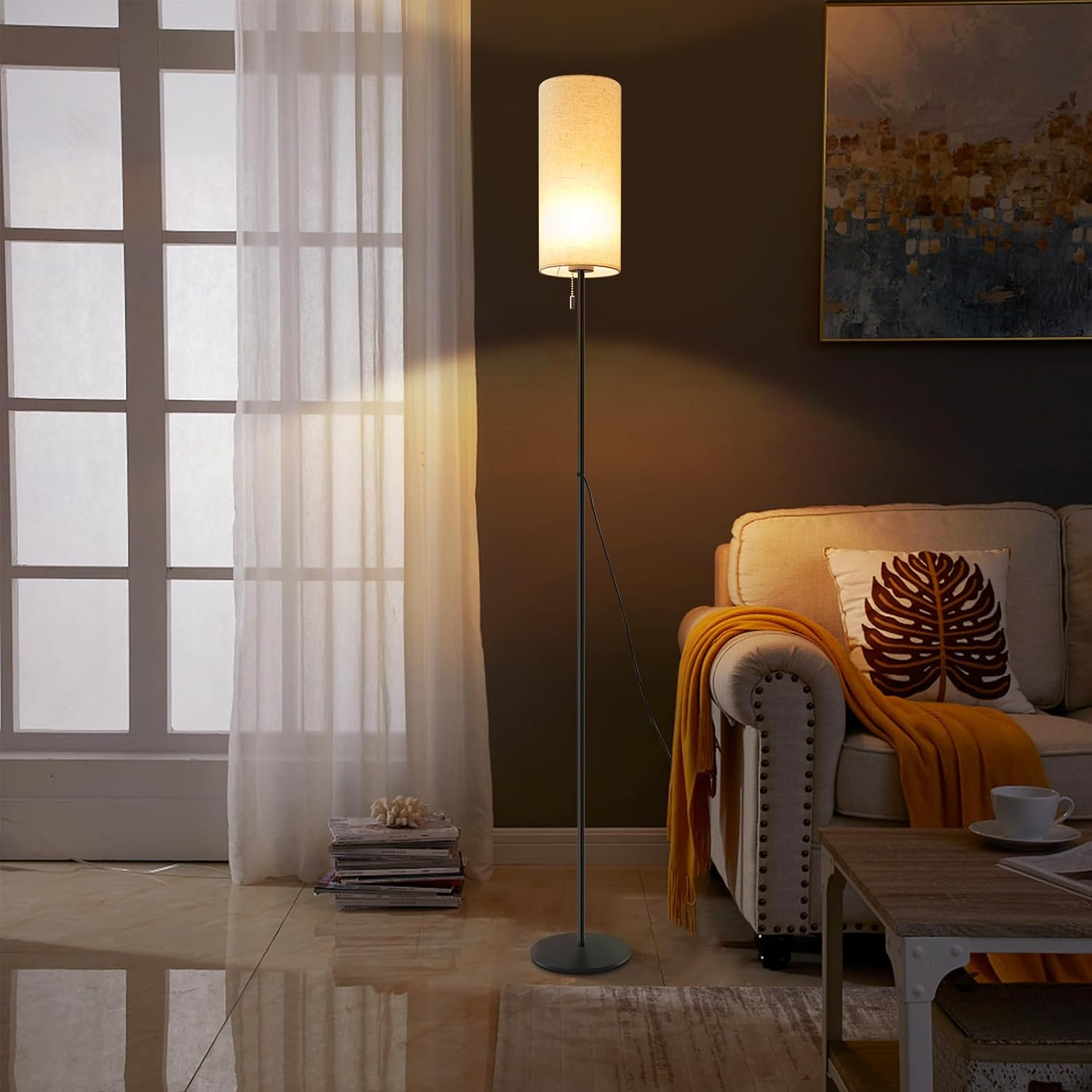 Wysoka lampa podłogowa z cylindrycznym kloszem, obok sofy i okna.
