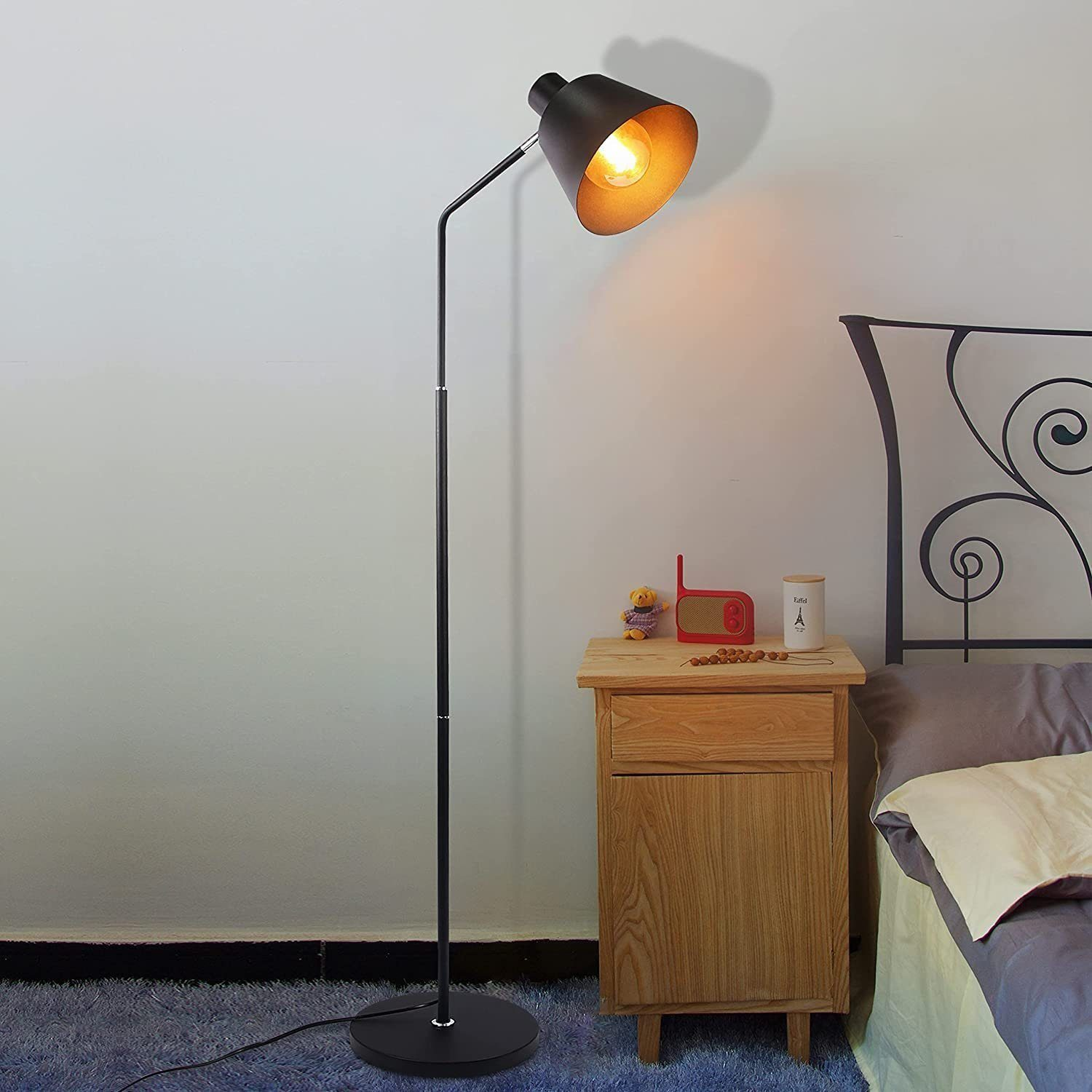 Eine schwarze Stehlampe mit orangenem Licht in einem Raum. Ein Nachttisch aus Holz ist vorhanden.