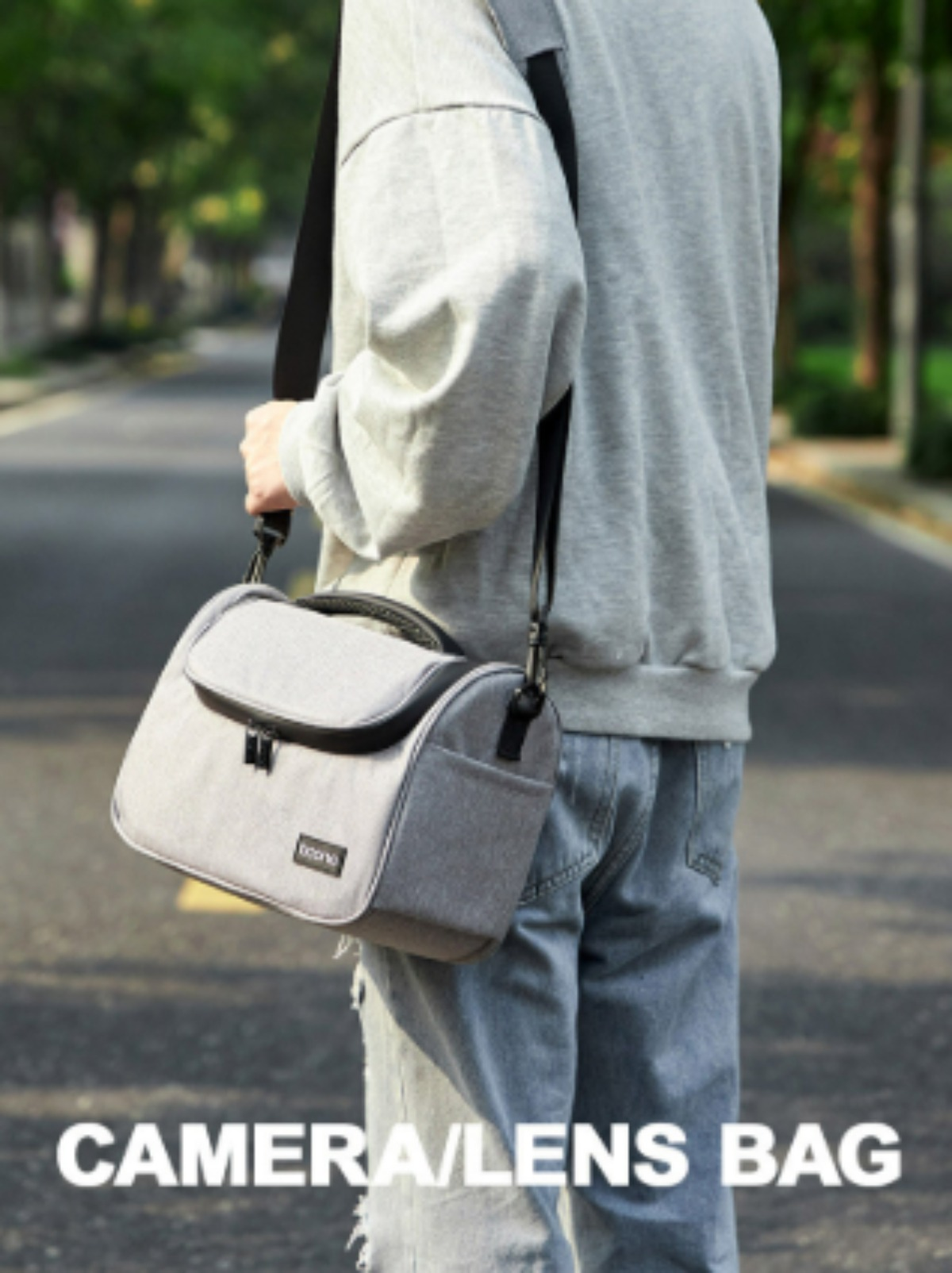 Person mit einer Kameratasche über der Schulter. Die Tasche ist grau, die Person trägt Freizeitkleidung.