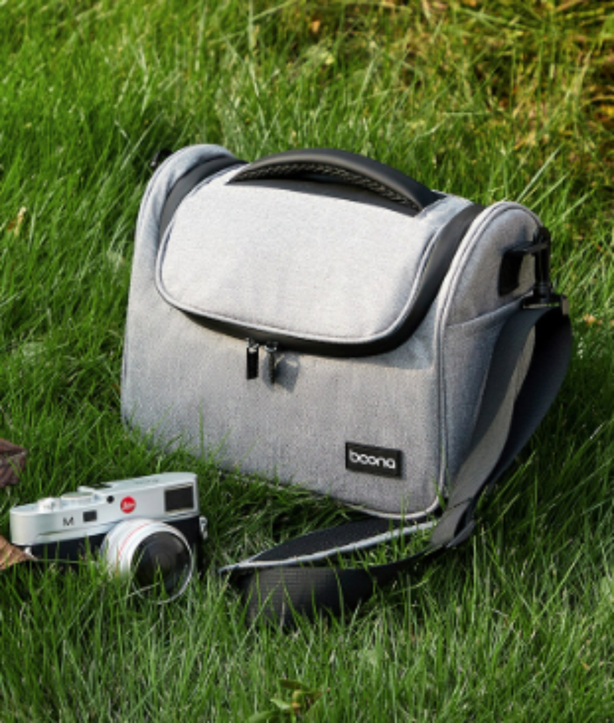 Graue Kameratasche auf Gras. Eine Kamera befindet sich neben der Tasche.