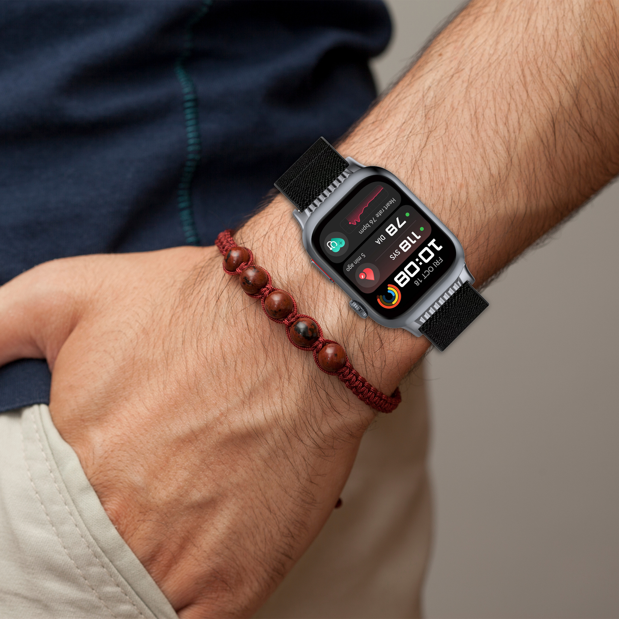 Un polso con uno smartwatch che mostra dati sanitari e un braccialetto con perline rosso scuro.