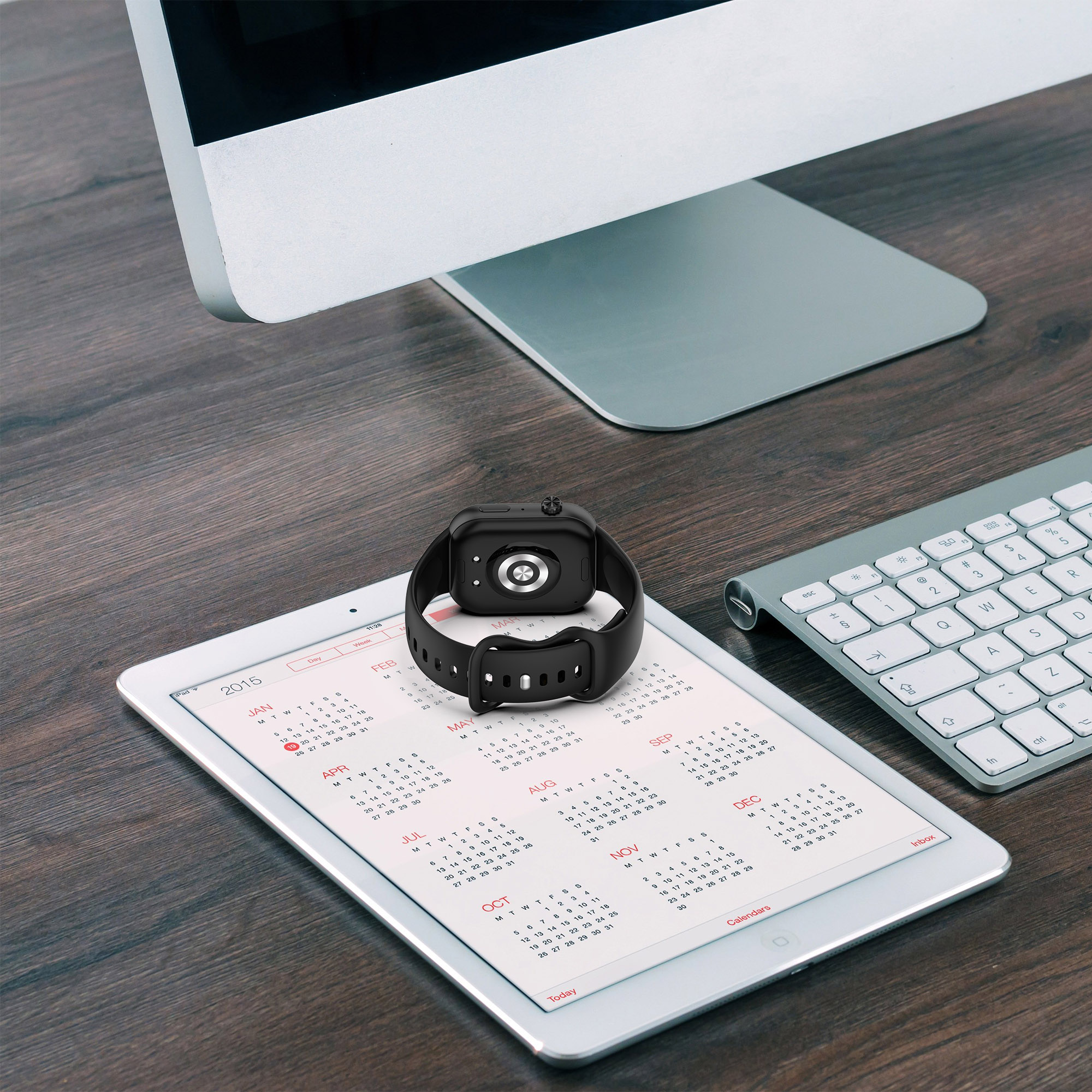 Eine schwarze Smartwatch auf einem weißen Tablet mit Kalender, neben einer Tastatur.