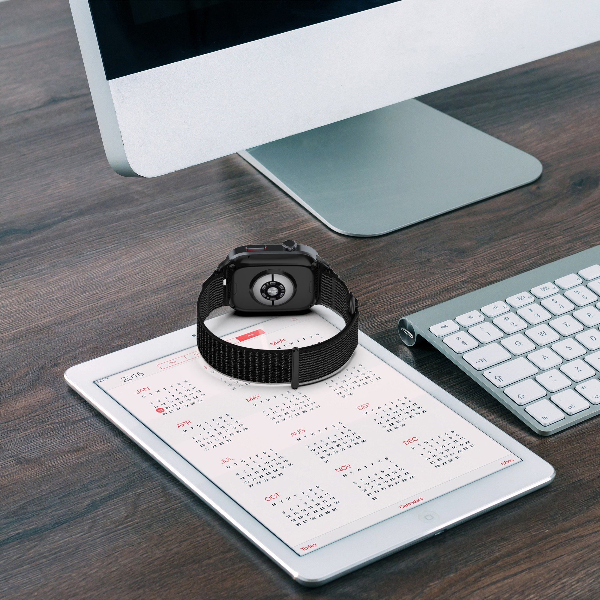 Smartwatch mit schwarzem Armband auf Tablet mit Kalender, Tastatur und Monitor.