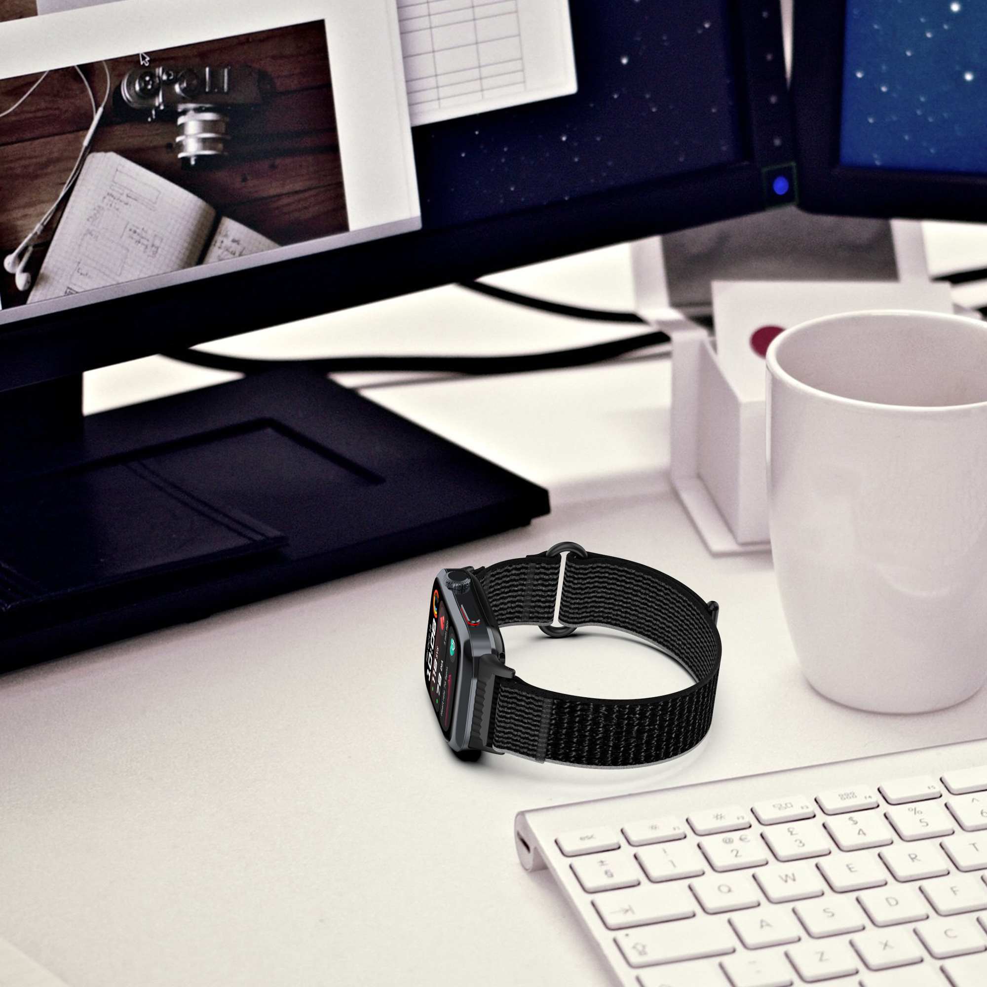 Schwarze Smartwatch mit schwarzem Band auf einem weißen Schreibtisch, Monitore und Tastatur im Hintergrund.