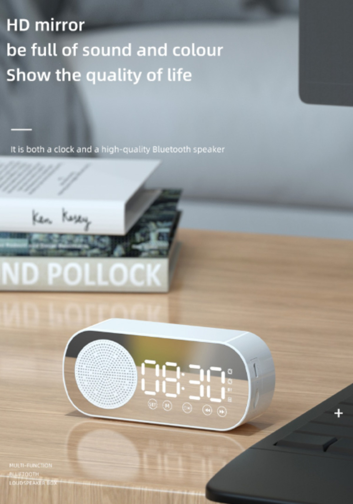 Eine weiße Digitaluhr und ein Lautsprecher auf einer Holzoberfläche mit Büchern und einem Laptop.