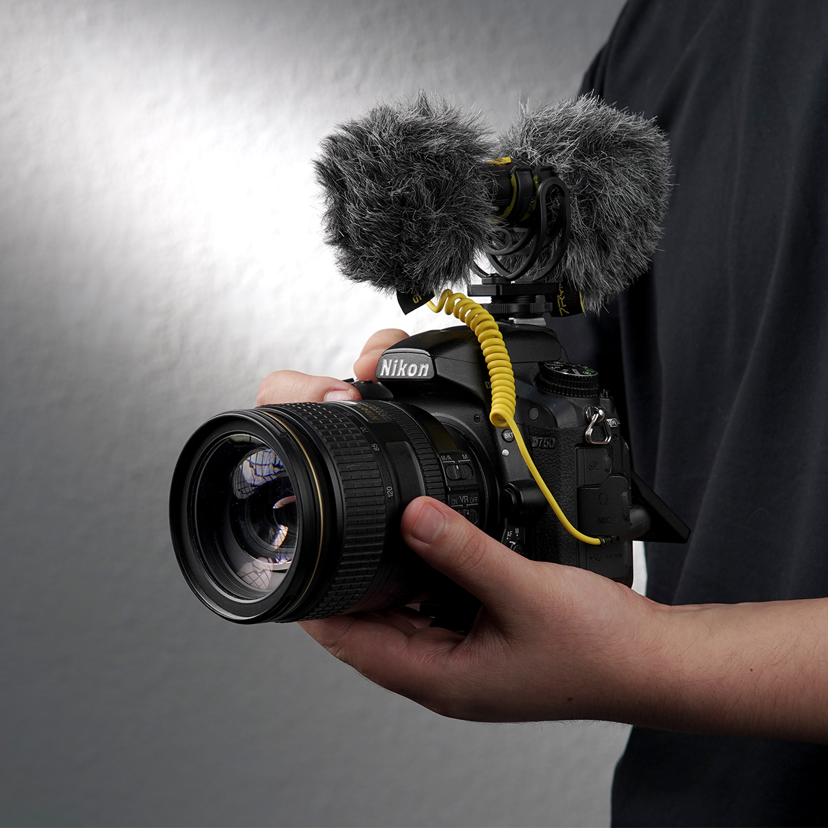 A person holding a camera with an attached microphone and a yellow cable.