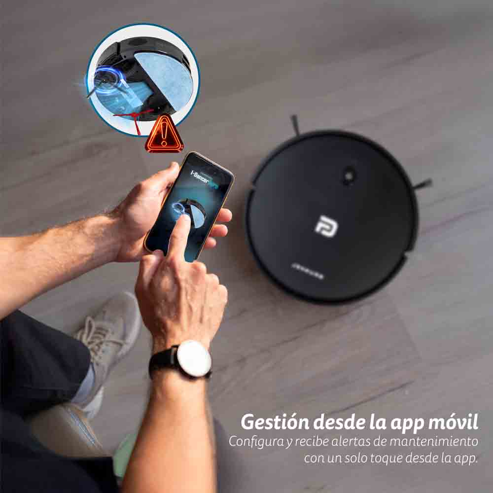 Una persona usando un teléfono y una aspiradora robótica en el suelo.