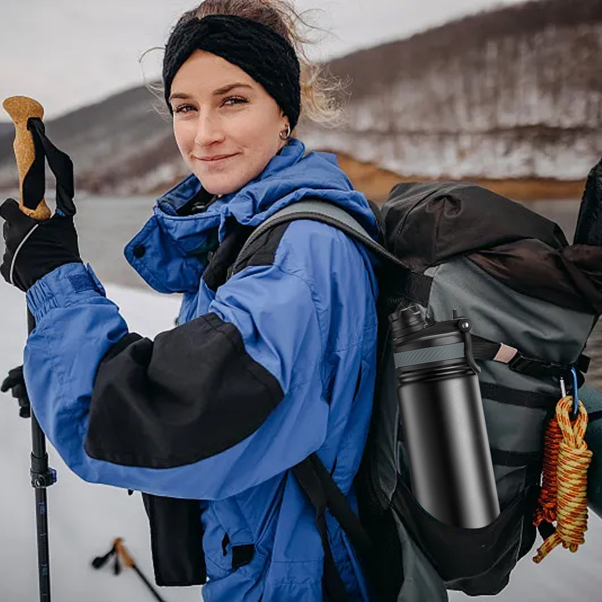 Eine Frau in Winterkleidung mit Wasserflasche und Wanderstock lächelt.