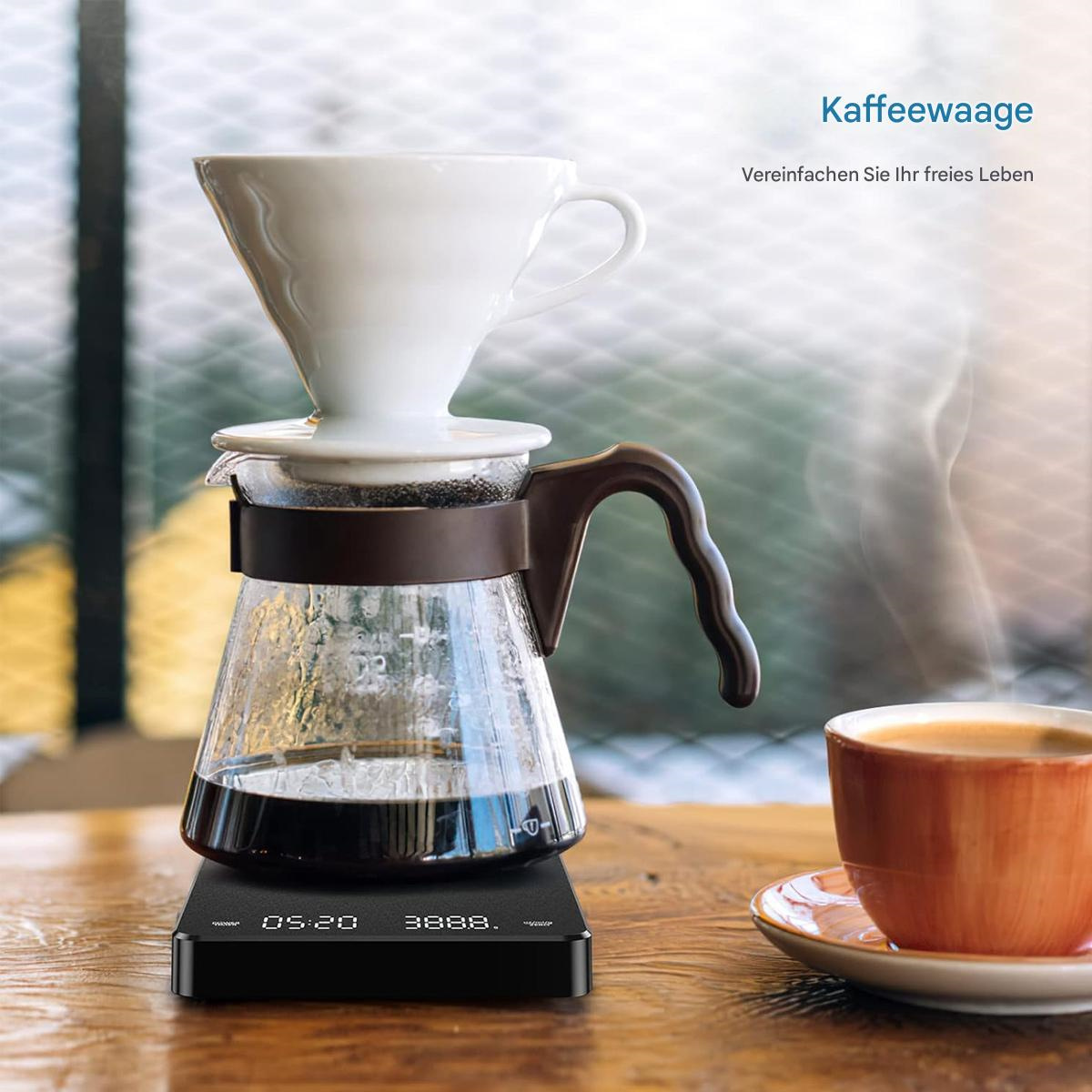 Ein Kaffee-Setup mit Waage, Glaskaraffe, Dripper und einer Tasse Kaffee. Dampf steigt auf.