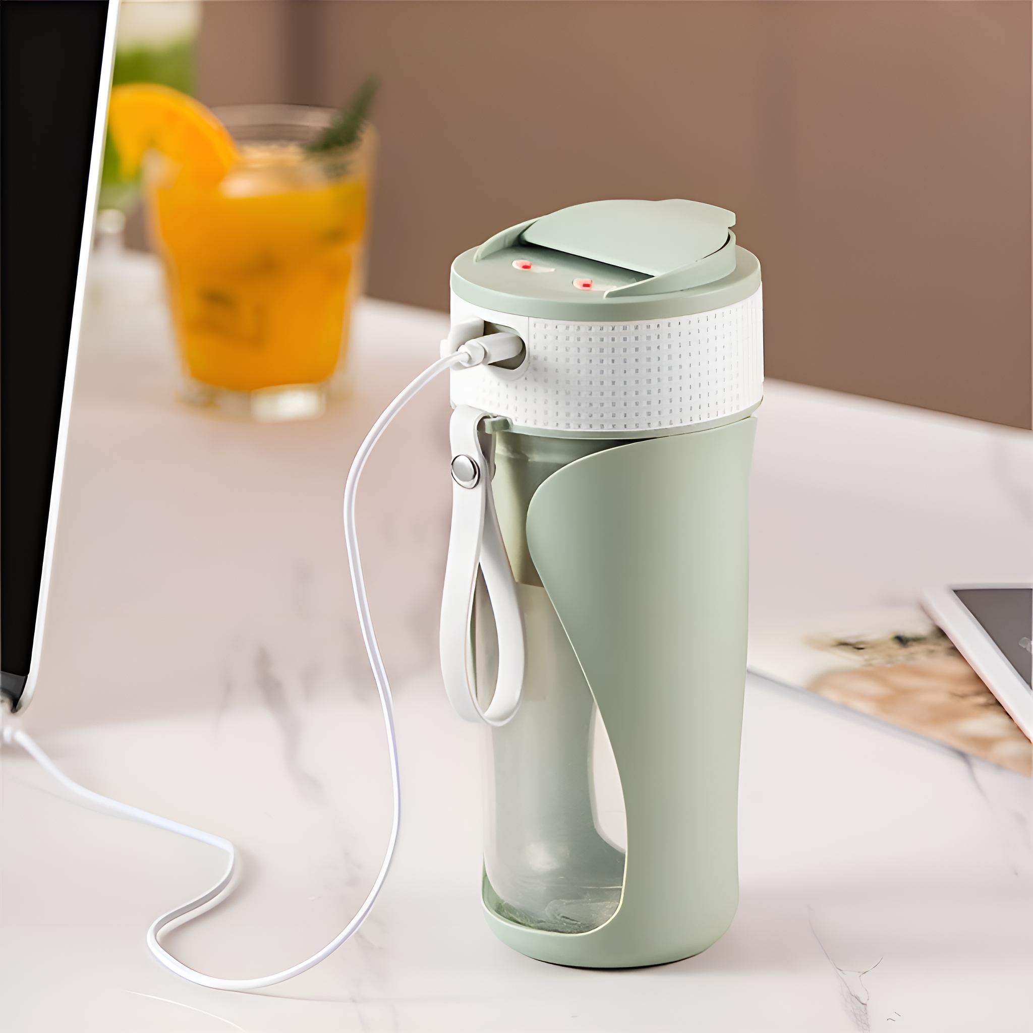 Grüner und weißer tragbarer Mixer mit Ladekabel und Glas Saft im Hintergrund.