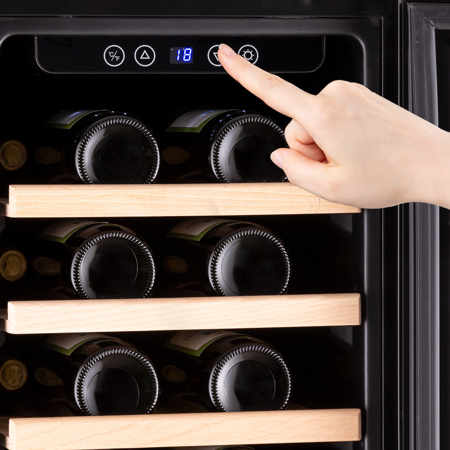 La mano di una persona tocca il pannello di controllo di un frigorifero per vini con bottiglie di vino all'interno.