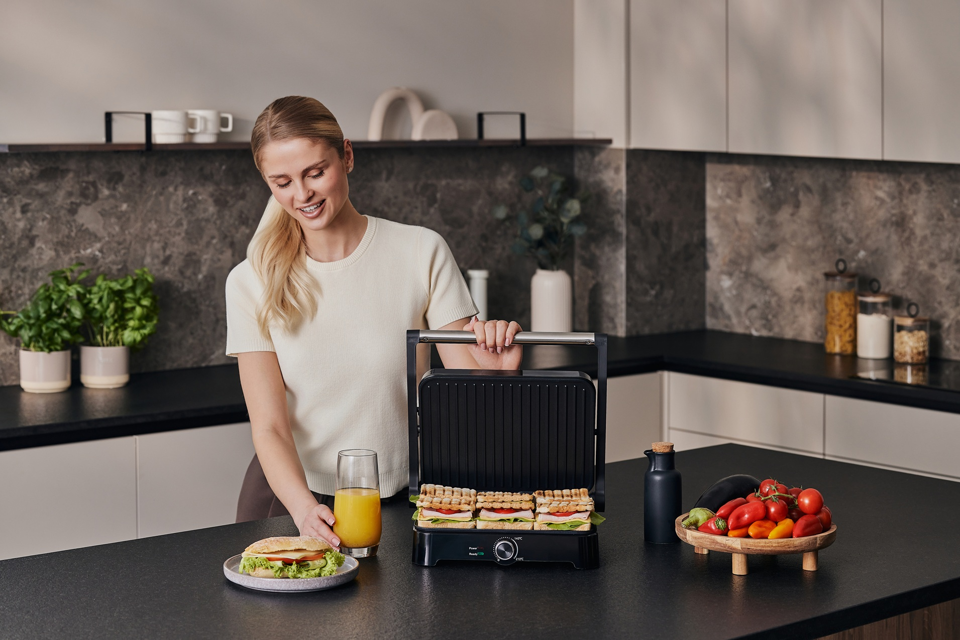 Eine Frau bereitet Sandwiches mit einem Grill zu, mit Zutaten auf dem Tisch.