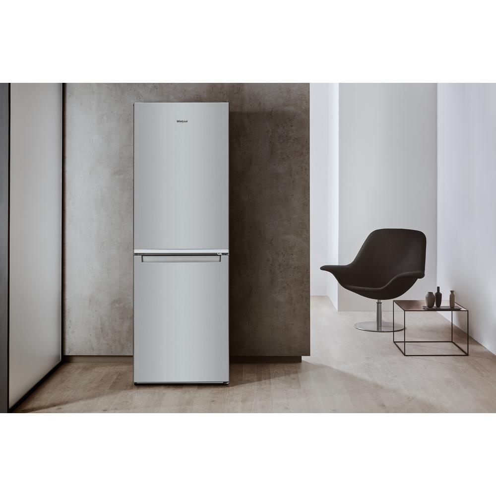Frigorifero Whirlpool argento con congelatore inferiore, contro un muro grigio testurizzato.