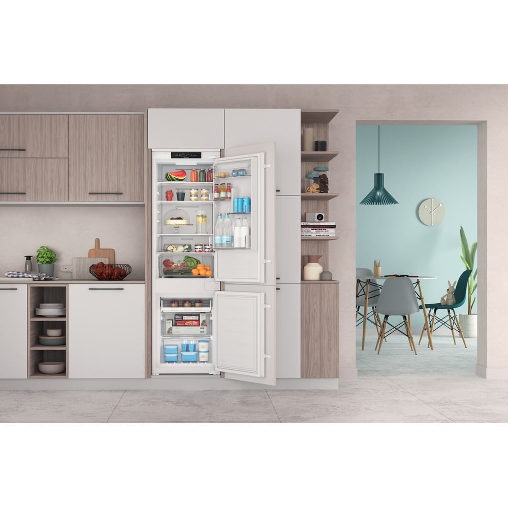 Refrigerador abierto con comida. Fondo de cocina con armarios y comedor es visible.