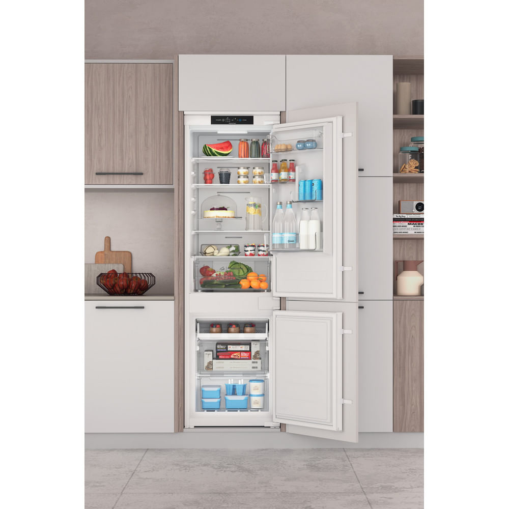 Un refrigerador abierto lleno de comida. El refrigerador está empotrado y tiene dos secciones.
