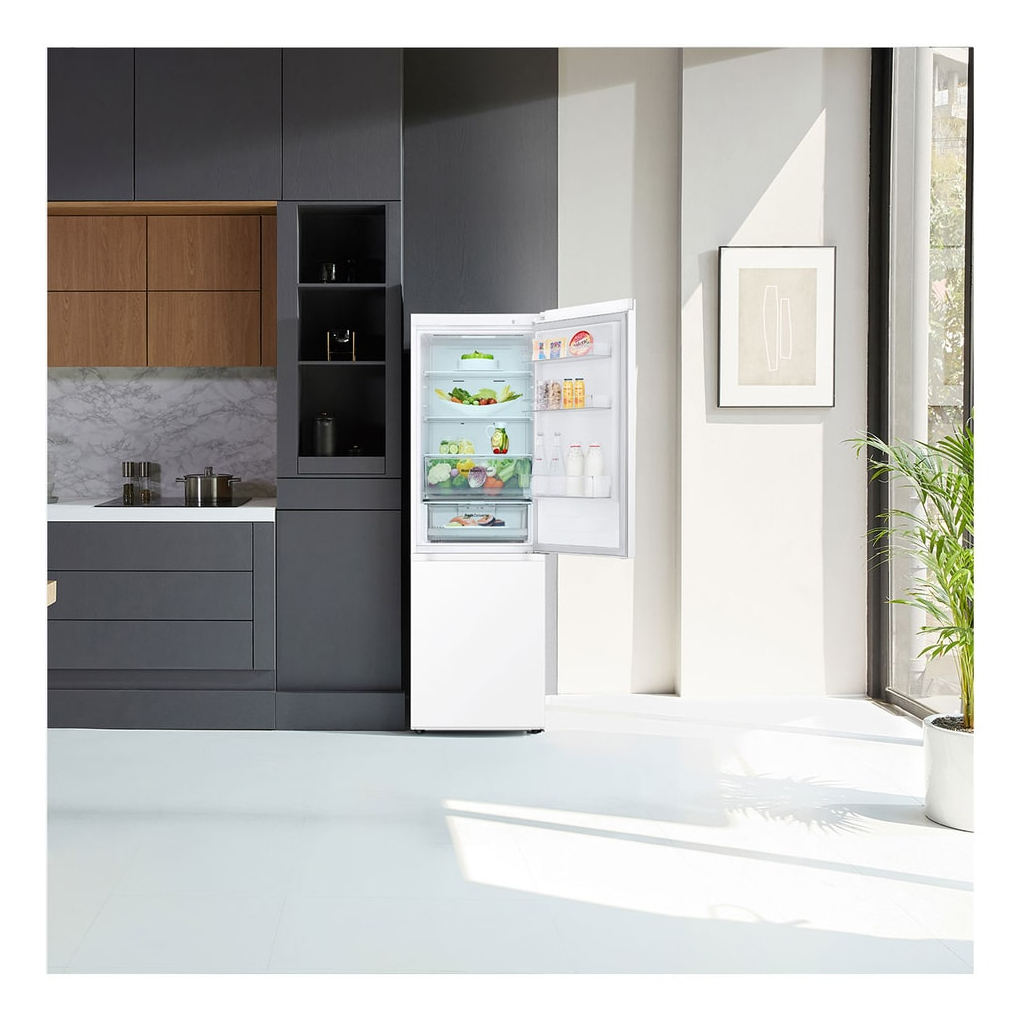 Biała lodówka w nowoczesnej kuchni. Otwarta, odsłaniająca jedzenie. Szare i drewniane szafki w tle.