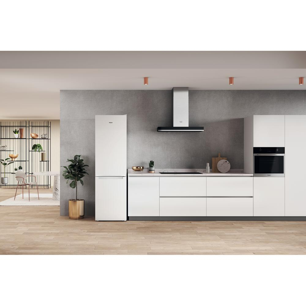 Cocina moderna con armarios blancos, electrodomésticos y suelo de madera. Una planta verde en una maceta a la izquierda.