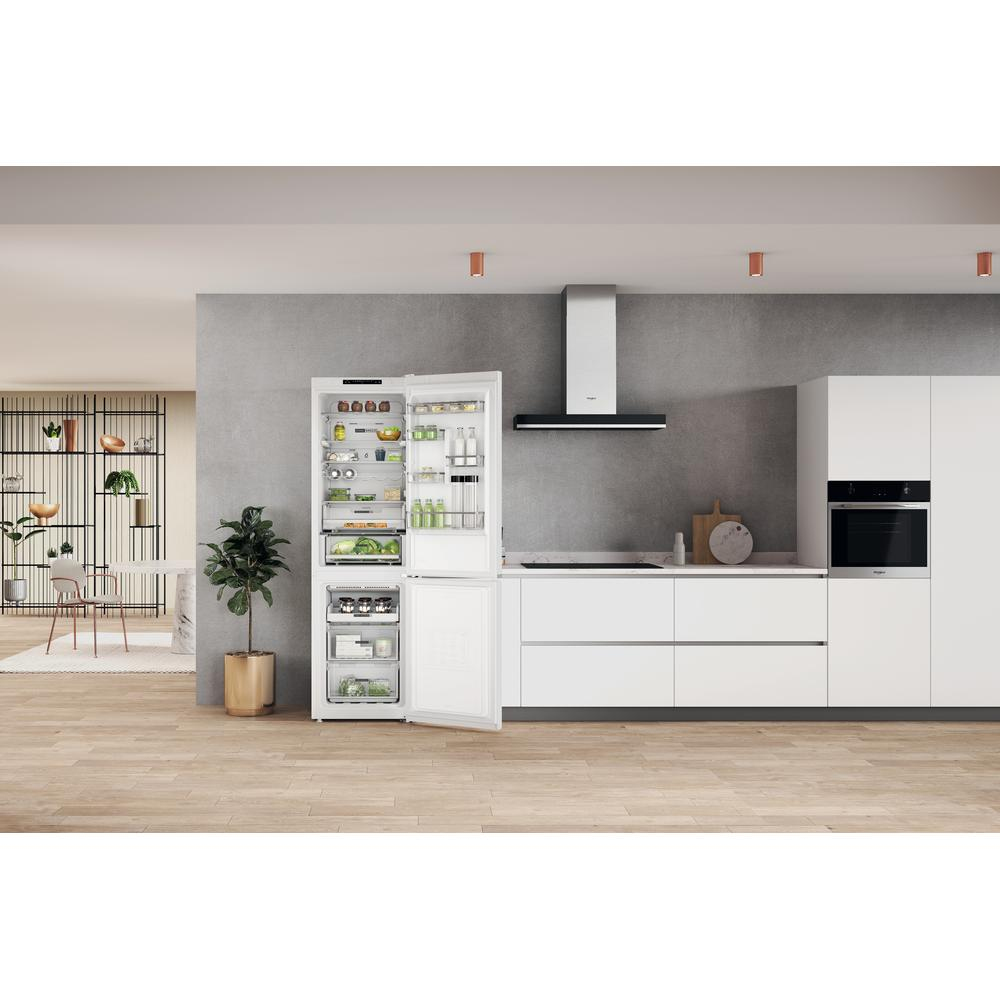 Interior de cocina con refrigerador abierto. Gabinetes blancos, piso de madera, pared gris y planta en maceta.