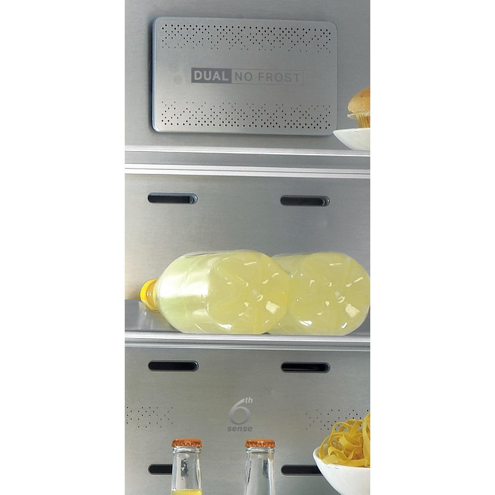 Interior del refrigerador con estantes. Botellas de vidrio, frascos y alimentos almacenados. Etiqueta Dual No Frost presente.