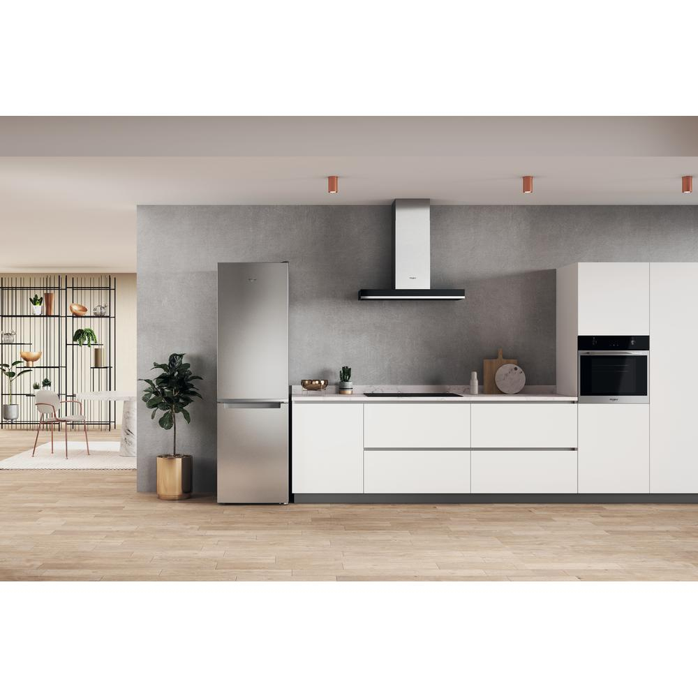 Cocina moderna con un refrigerador de acero inoxidable. Armarios blancos, suelo de madera y pared gris son visibles.