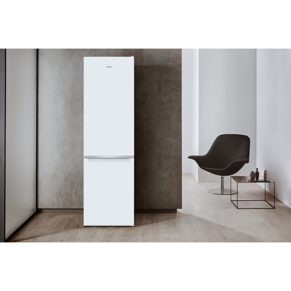 Frigorífico blanco, cerrado, contra una pared gris, con una silla negra y mesa de cristal.