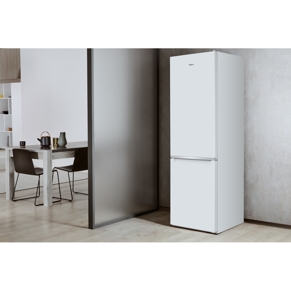 Un refrigerador blanco junto a una pared gris, una mesa de comedor y sillas.