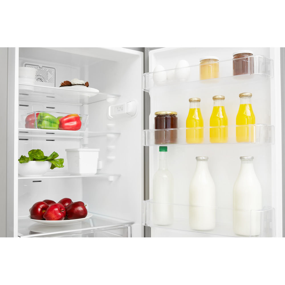Interior de refrigerador. Estantes con comida, incluyendo manzanas rojas, pimientos y botellas de jugo.