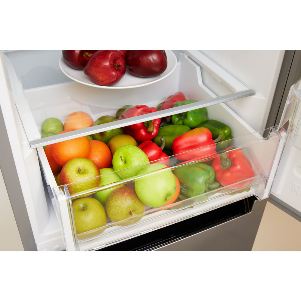 Cajón del refrigerador lleno de productos. Manzanas, naranjas, pimientos y peras. Fondo blanco.