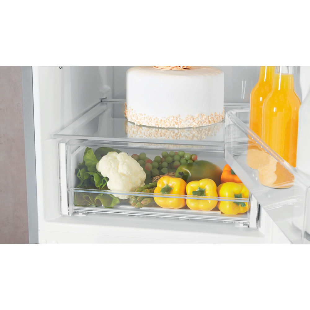 Cajón de refrigerador lleno de verduras, pastel y botellas de jugo. Cajón transparente.