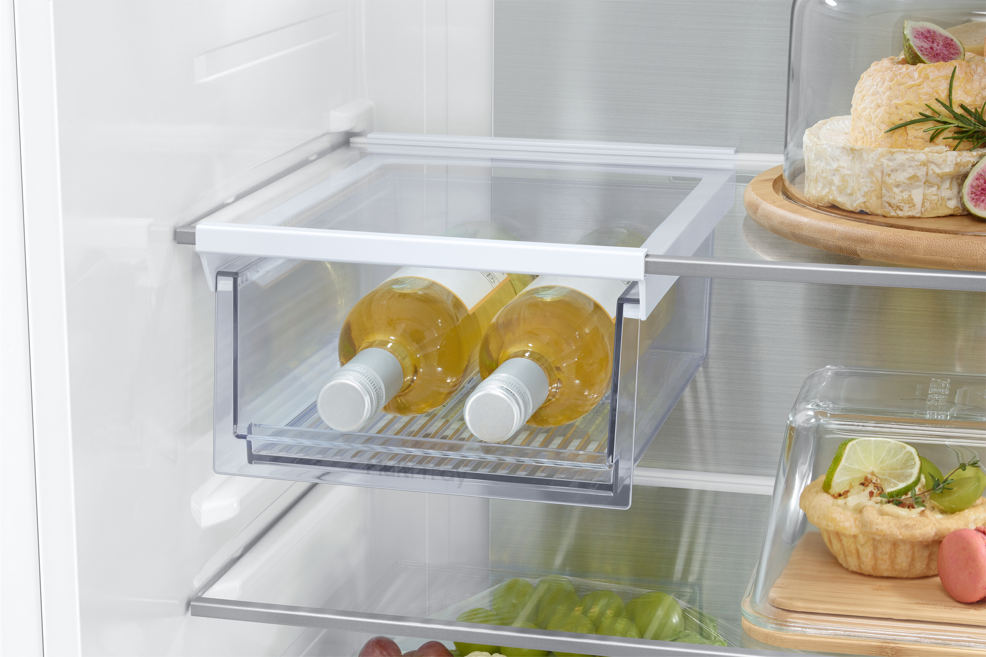 Im Inneren des Kühlschranks. Zwei Weinflaschen befinden sich in einer Schublade. Etwas Käse und Dessert.