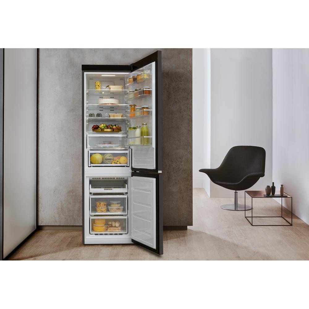 Refrigerador abierto en una habitación. Contenido visible. Silla y mesa auxiliar al lado. Paredes blancas.