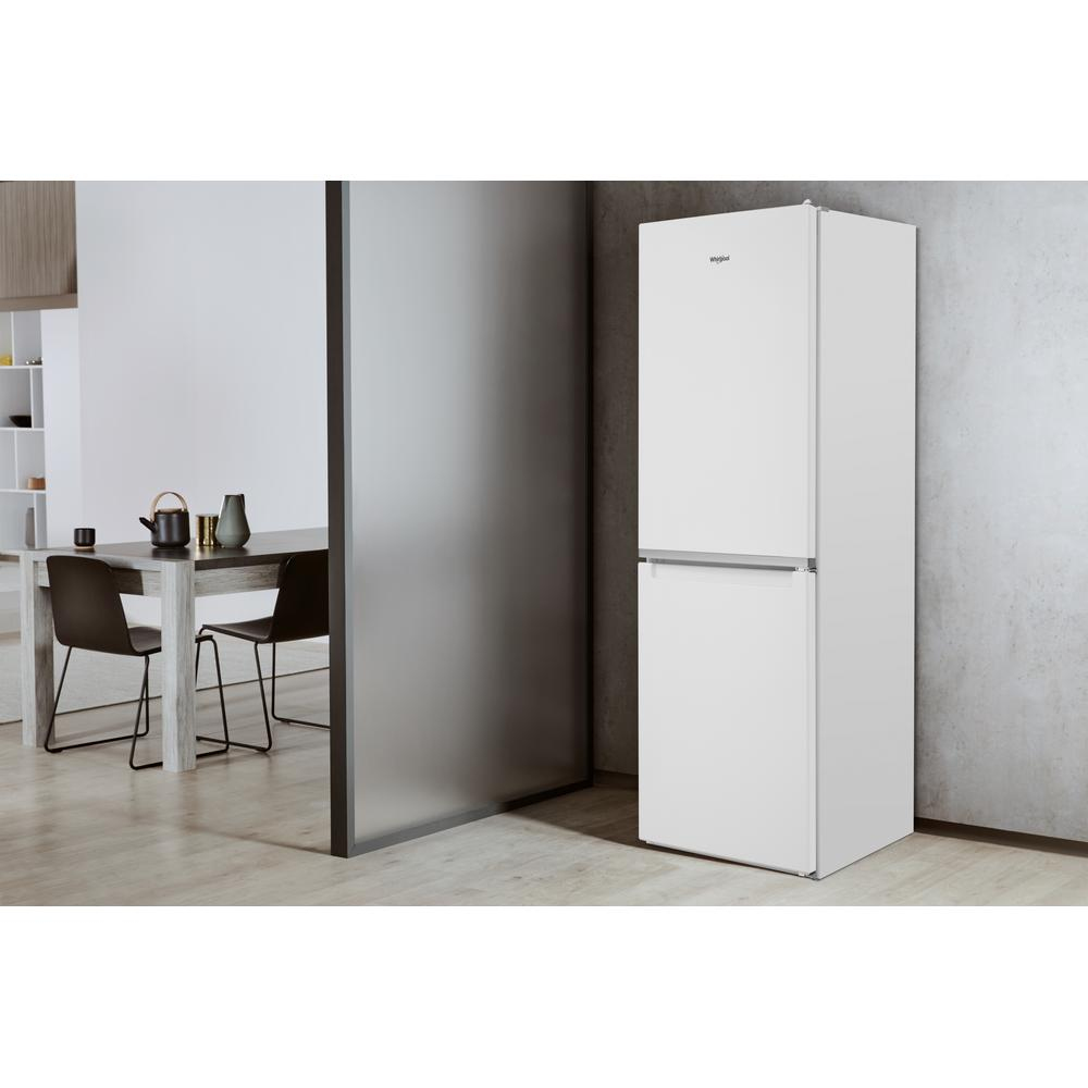 Un frigorifero Whirlpool bianco con due porte è accanto a un muro grigio e un pavimento in legno.