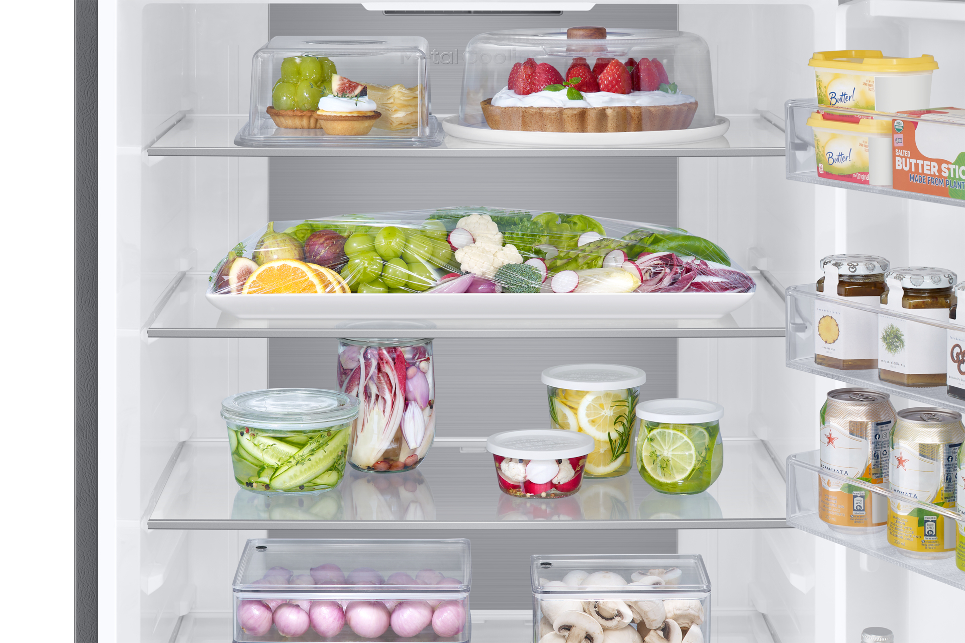 Wnętrze lodówki wypełnione jedzeniem. Są półki z owocami, warzywami i pakowanymi produktami spożywczymi. Białe wnętrze.