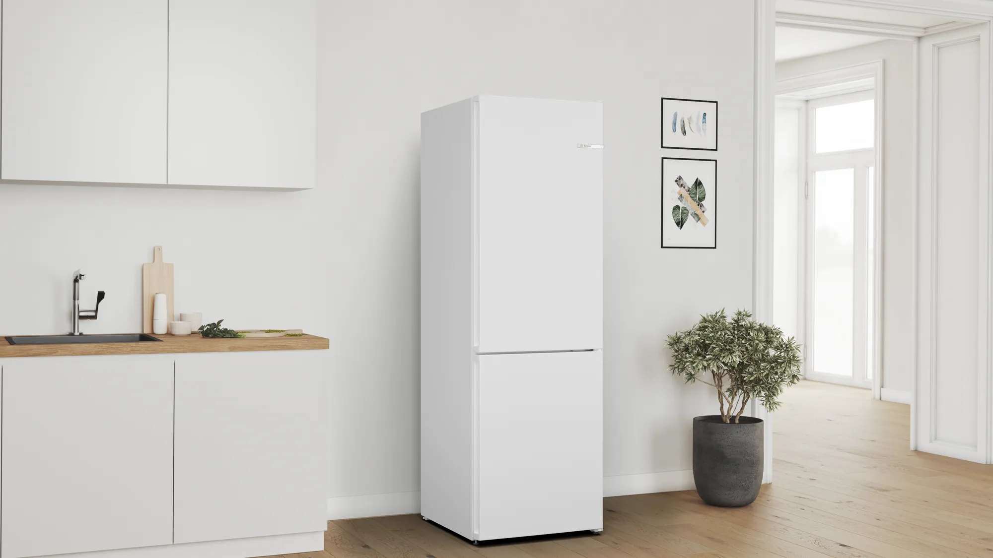 Witte koelkast in een witte keuken. Minimalistisch ontwerp. Keukenblad en plant zijn zichtbaar.
