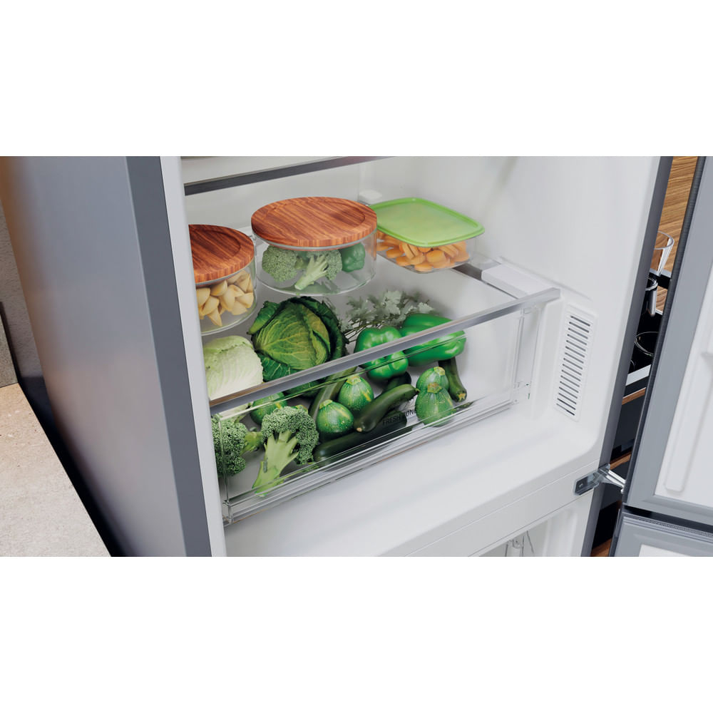 Interior de refrigerador con cajones llenos de verduras y frutas frescas. Varios recipientes son visibles.
