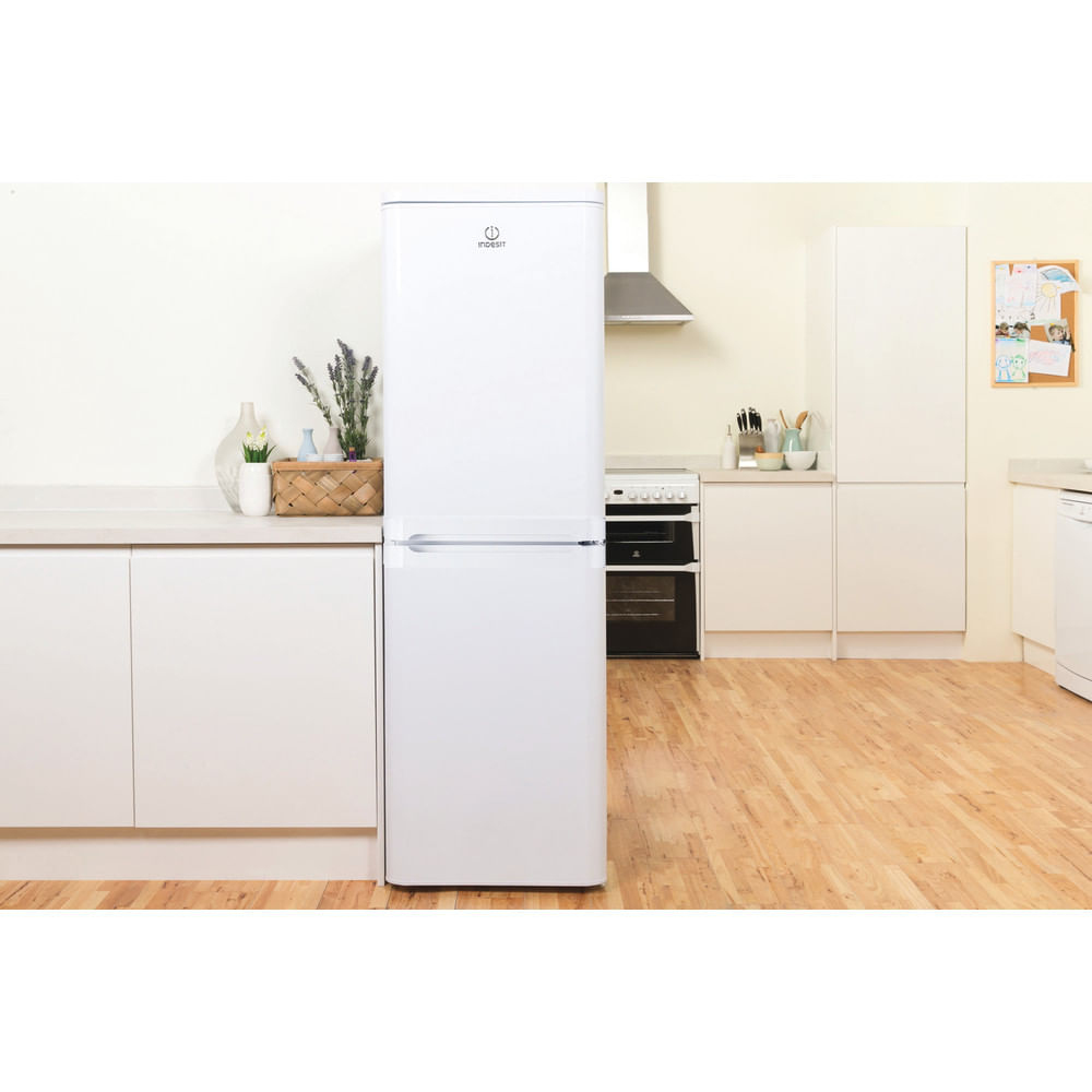 Un refrigerador Indesit blanco en una cocina luminosa. Es un modelo de dos puertas, contra una pared blanca.