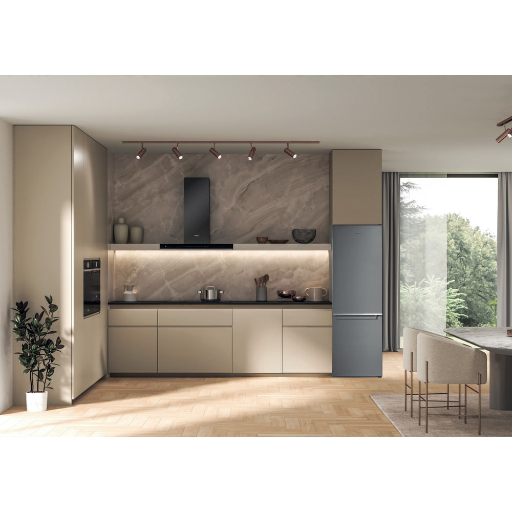 Cucina moderna con mobili beige, frigorifero grigio e finestra con verde. Una pianta a sinistra.