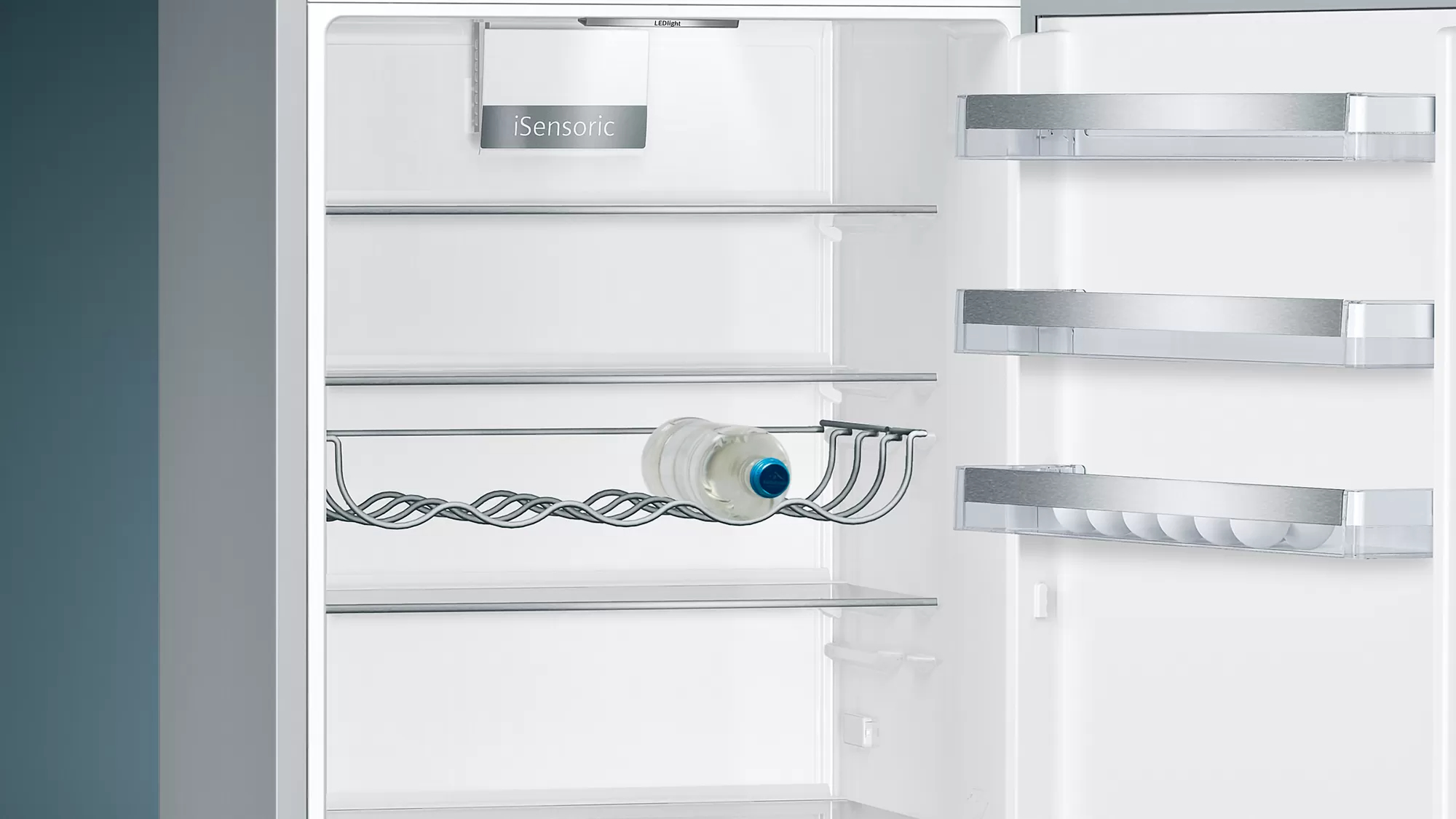 In einem Kühlschrank. Eine Wasserflasche steht in einem Drahtgestell. Regale sind sichtbar.