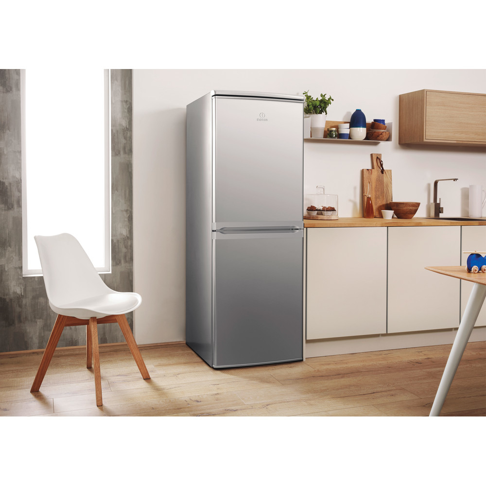 Un refrigerador plateado en un entorno de cocina, con una silla blanca en primer plano.