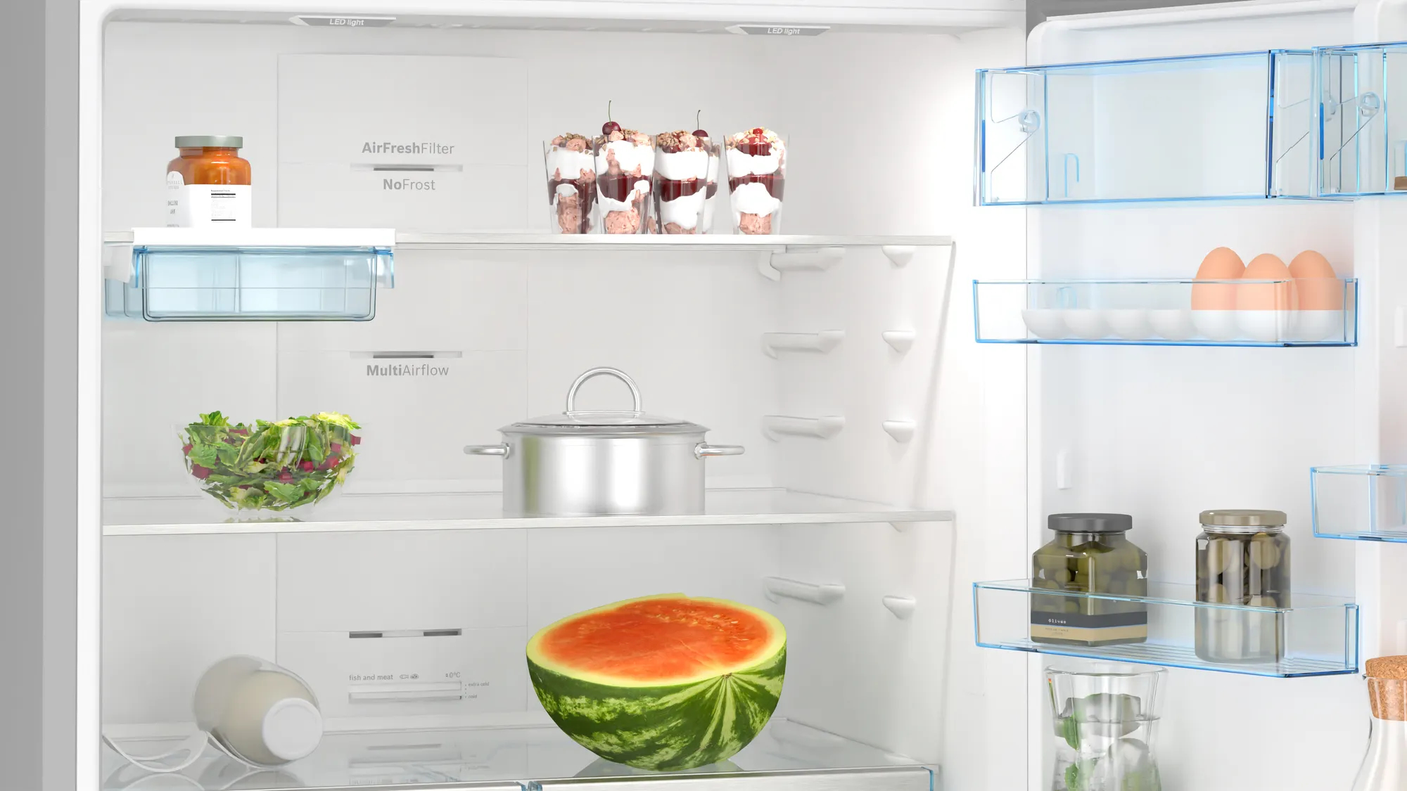 Das Innere eines weißen Kühlschranks. Lebensmittel befinden sich im Kühlschrank, darunter eine Wassermelone und Salat.
