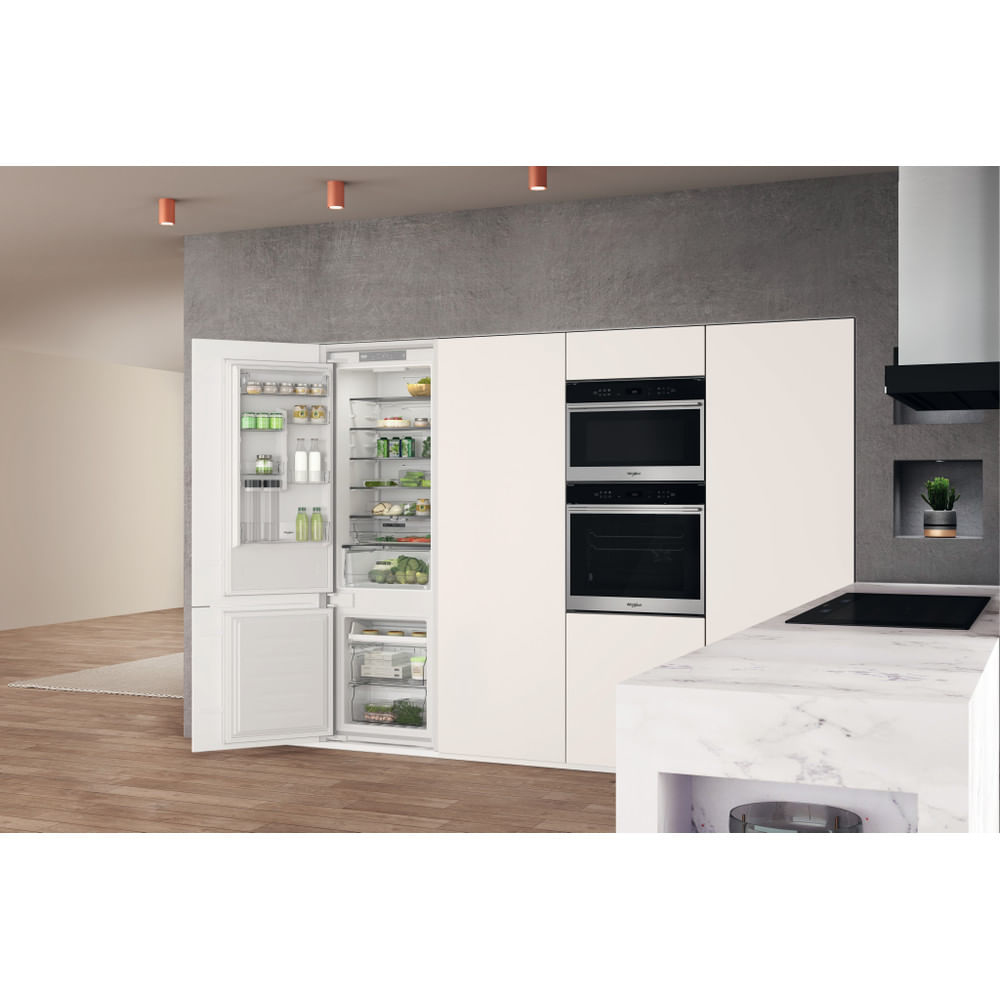 Cocina con refrigerador abierto, hornos y encimera de mármol. Suelo de madera y luces empotradas.