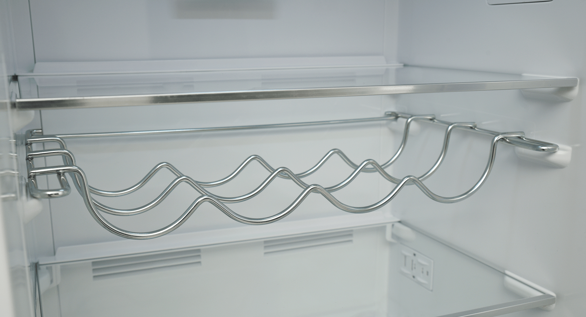 Wewnątrz lodówki zamontowany jest metalowy stojak na wino. Nad nim pusta półka.