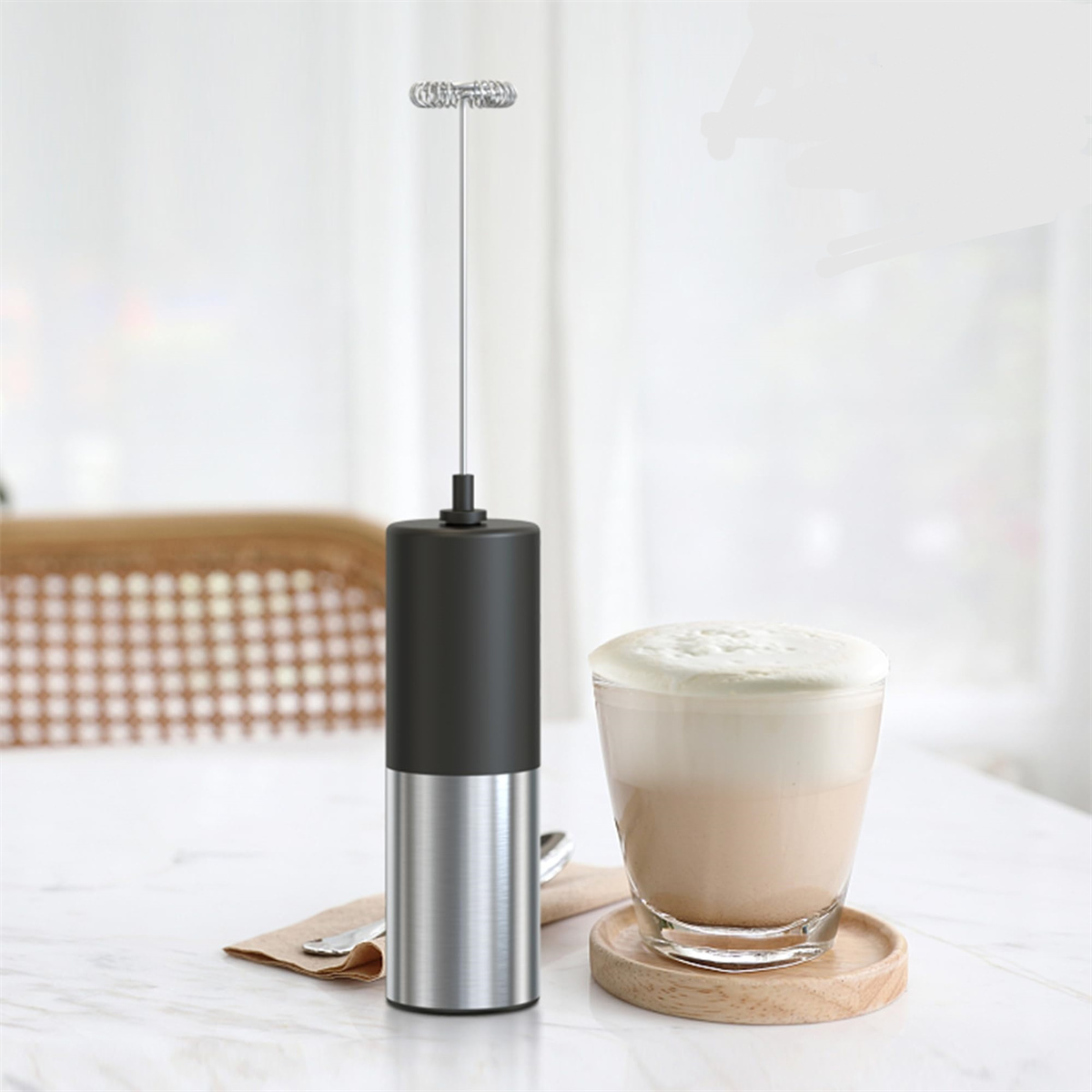 Ein Milchaufschäumer mit einer Tasse schaumigem Latte auf einem Holzuntersetzer.