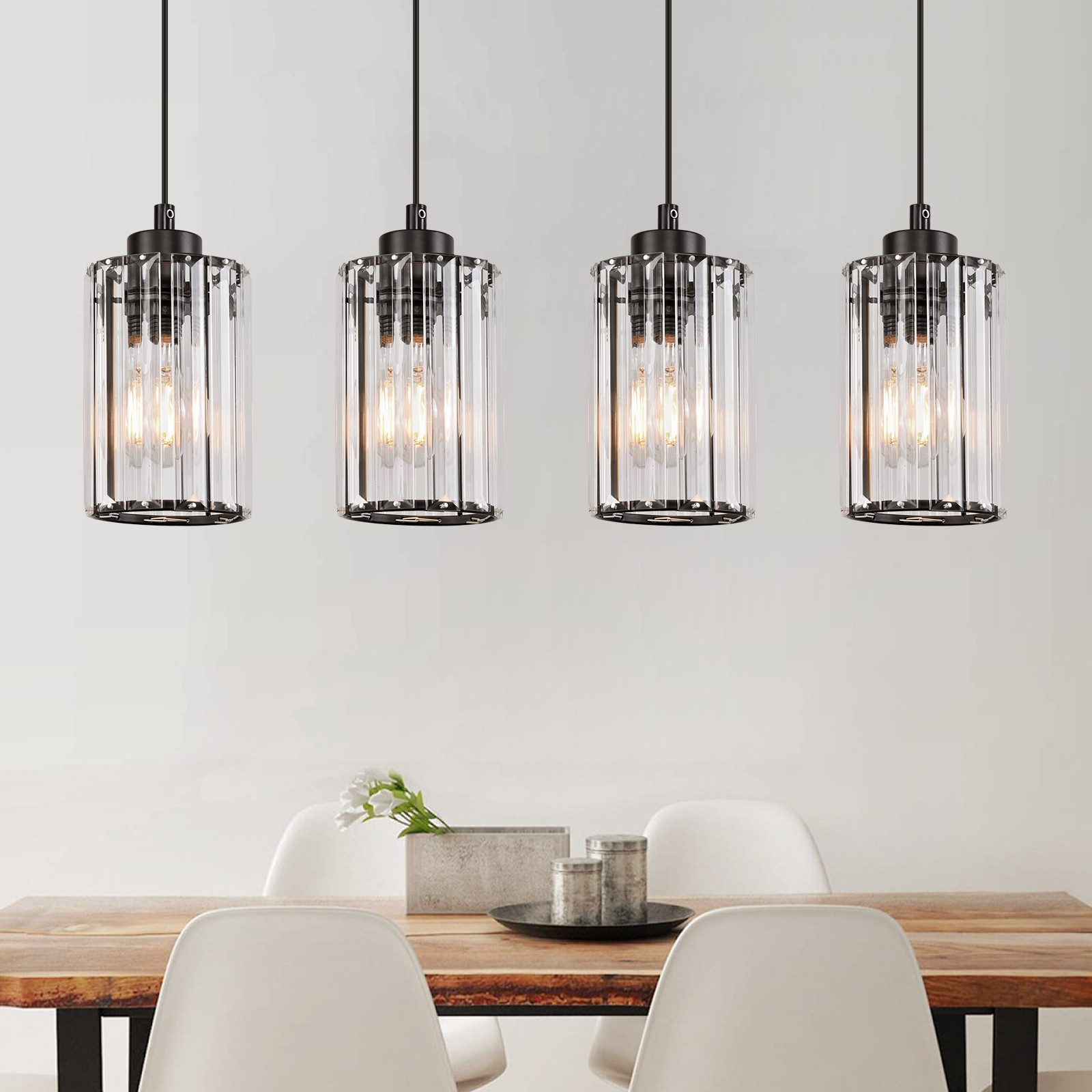 Cztery lampy wiszące z szklanymi kloszami wiszące nad drewnianym stołem, białe ściany.