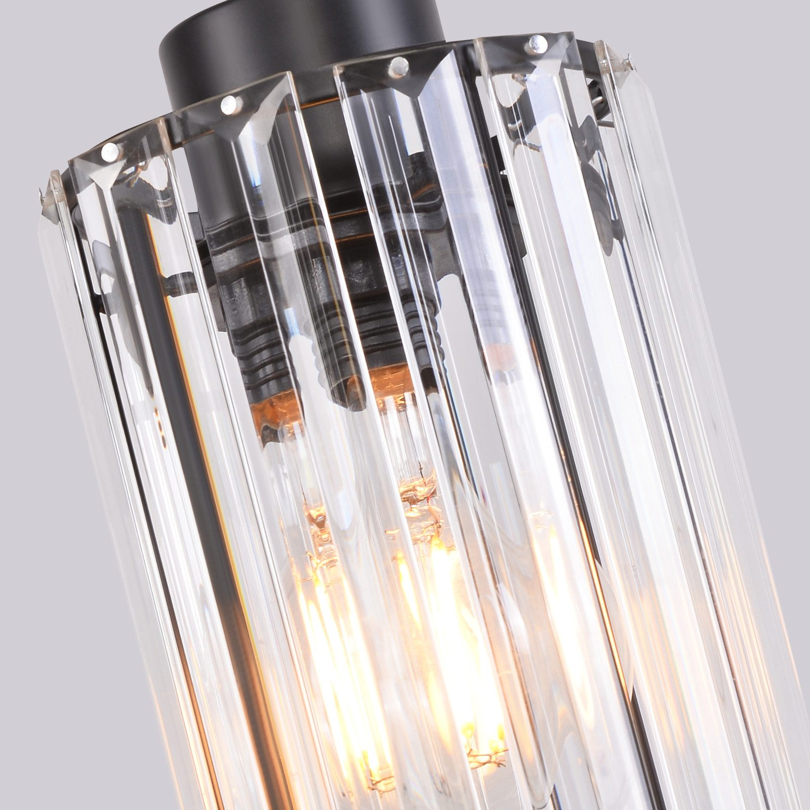 Zbliżenie przezroczystej cylindrycznej lampy z trzema widocznymi żarówkami. Lampa jest czarna u góry.