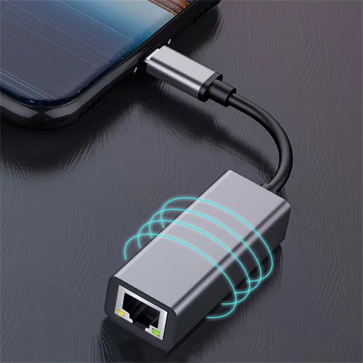 Ein grauer Ethernet-Adapter ist mit einem Telefon verbunden. Der Adapter hat einen Ethernet-Anschluss. Das Telefon liegt auf einer Oberfläche.