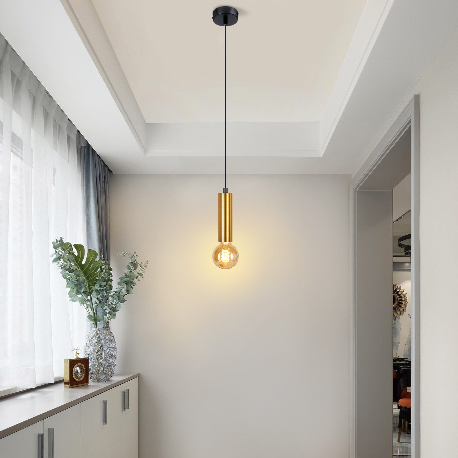 Eine goldene Pendelleuchte, die von der Decke in einem Flur hängt, mit einer weißen Wand und einer Tür.