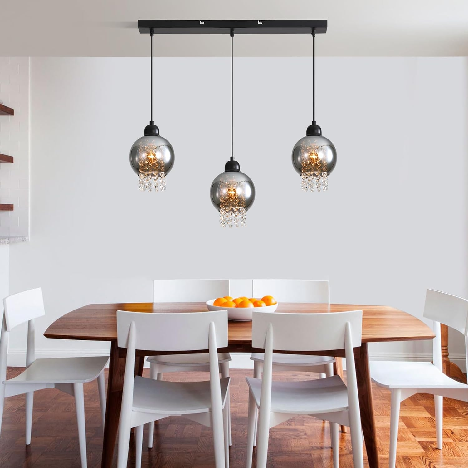 Comedor con tres luces de bola de cristal colgantes sobre una mesa de madera y sillas blancas.