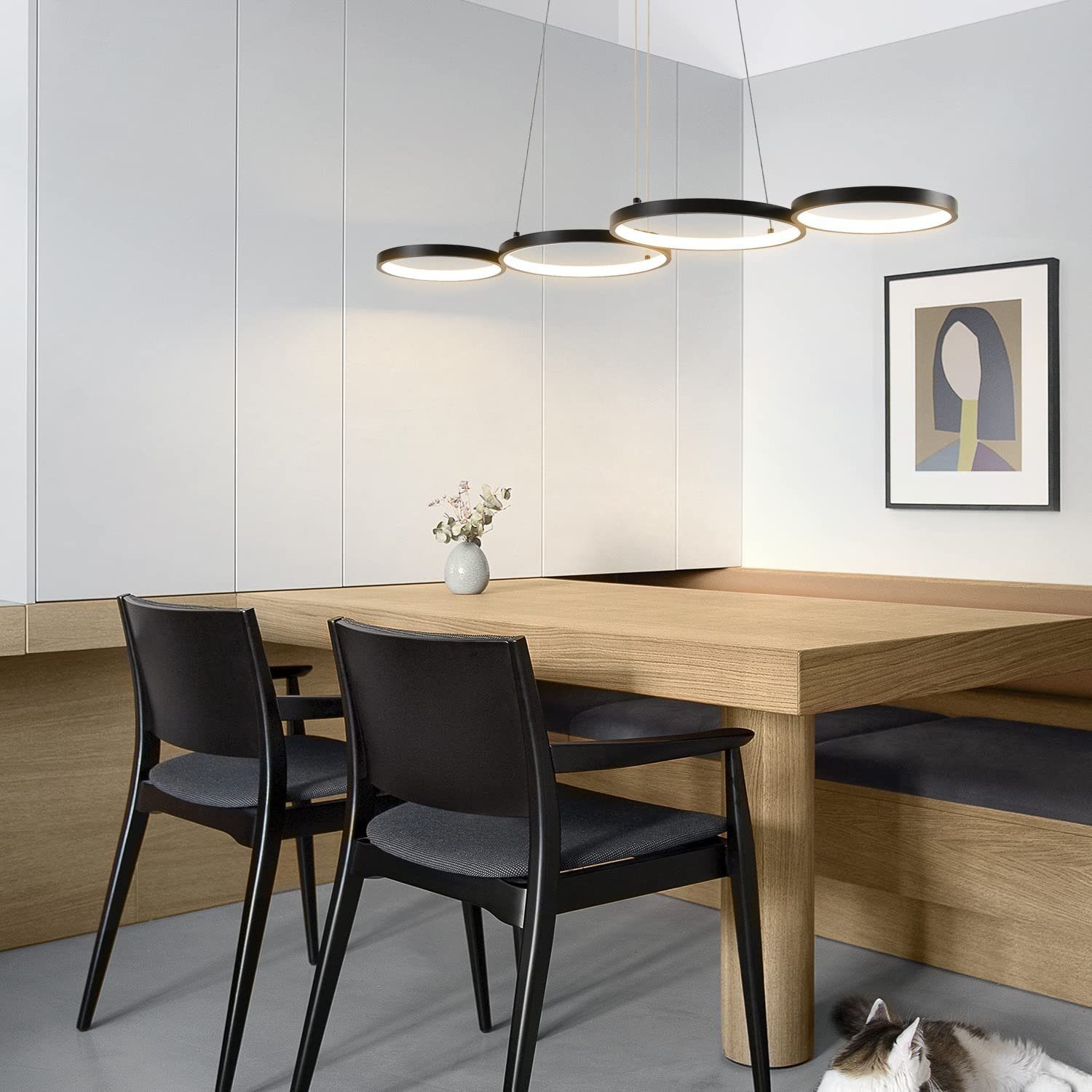 Ein Esszimmer mit Holztisch, schwarzen Stühlen, einem Bild und drei Ringlichtern.
