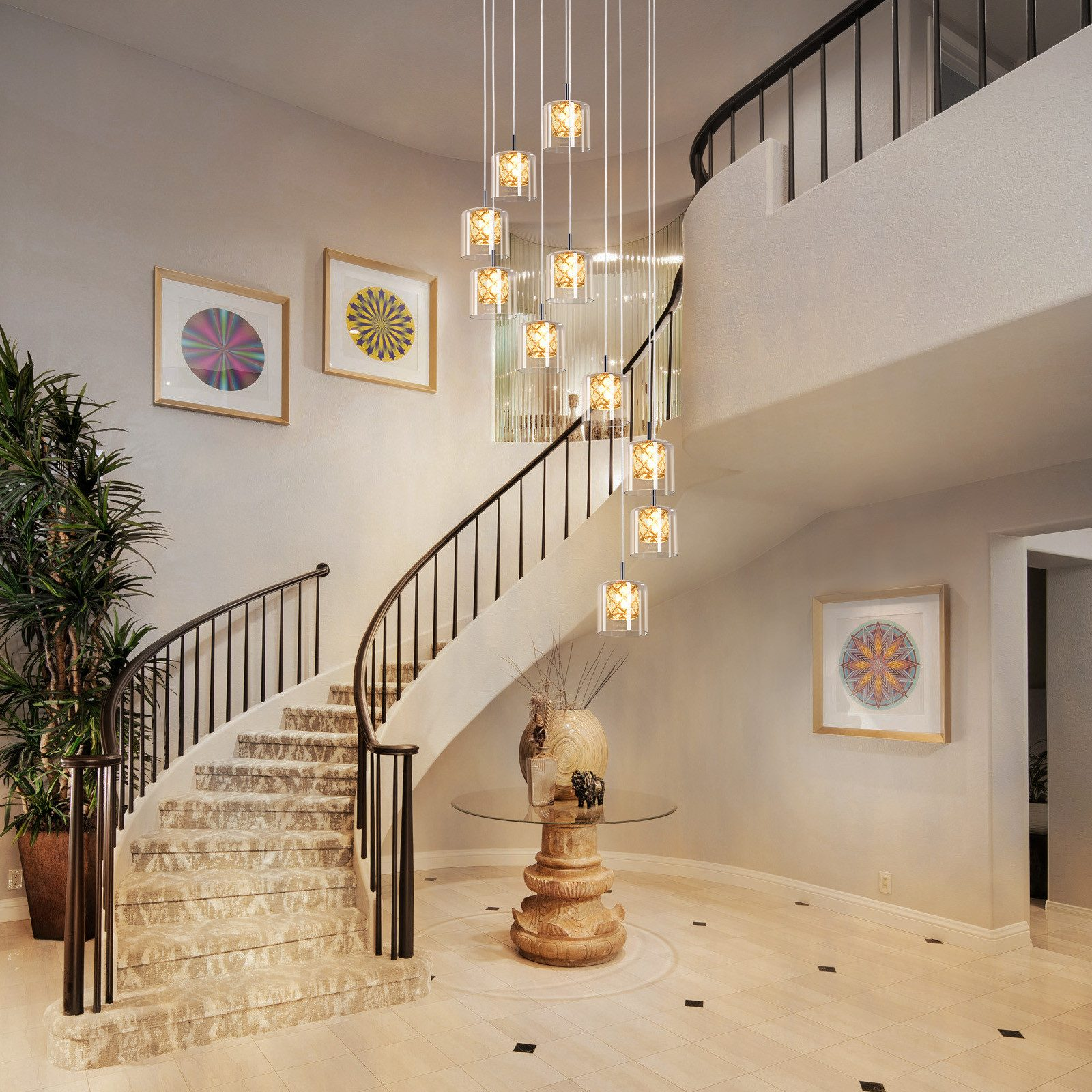 Eleganckie wnętrze: kręcone schody, żyrandol, dzieła sztuki, stół i duża roślina doniczkowa.
